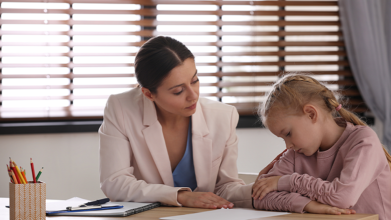 teacher and student sitting at a table looking at a piece of paper on the table