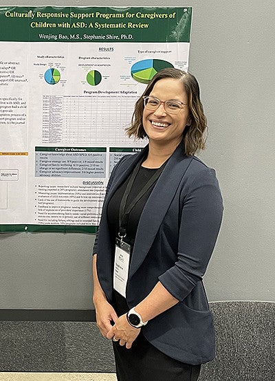 image of Stephanie Shire, PhD, standing in front of research poster facing camera