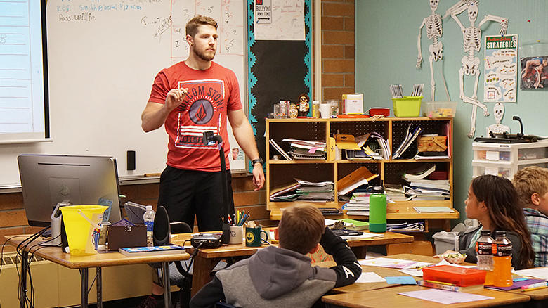 COE alumni teaching in a classroom with students sitting at a desk