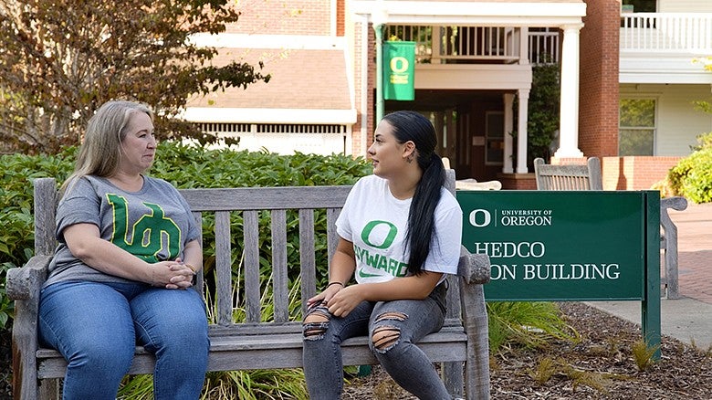 two students talking while sitting on a bench in front of HEDCO building