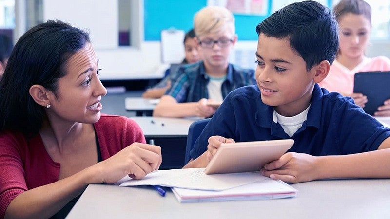 teacher kneeling talking to a student sitting at a desk