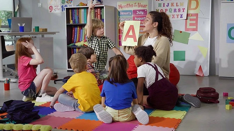 teaching sitting on floor holding up the letter A with a group of young individuals