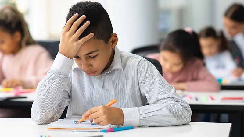 student looking down on desk with hand on their head