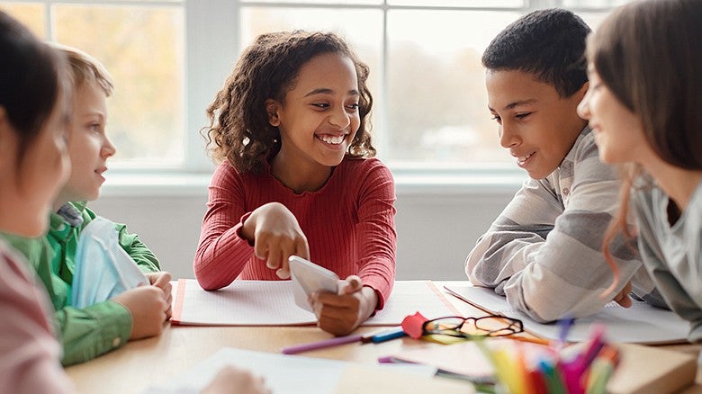 children sitting at a table looking at a cell phone while smiling