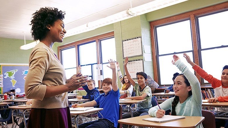 teacher in a classroom filled with children raising their hands