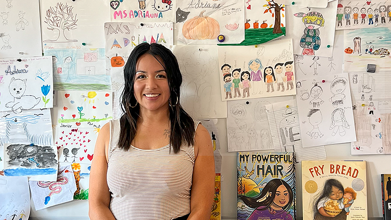 Adriana Alvarez standing in a classroom with children's drawings in the background