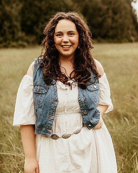 alumni Lily Smith standing in a field with trees in the background