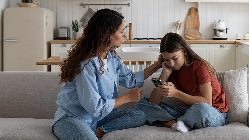 an adult talking to a young person who is looking down on their electronic device