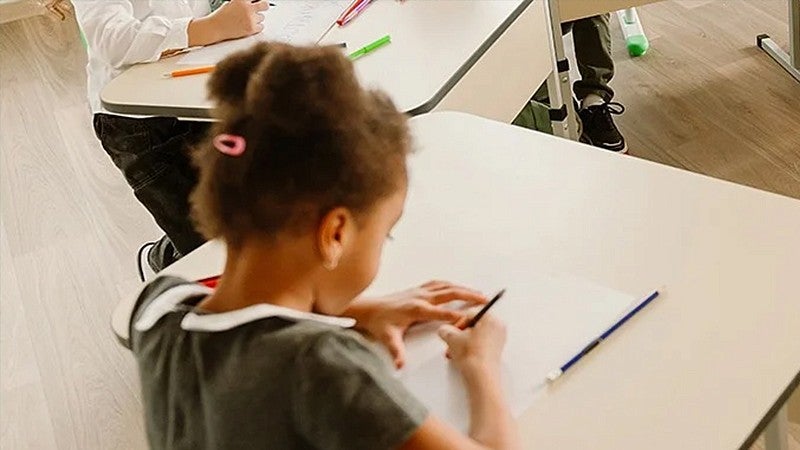 young individual in a classroom setting sitting at a desk writing