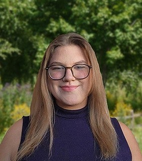 Kendra Ames smiling at the camera standing in front of a lush green background