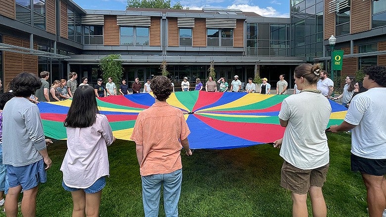 group of students holding onto a rainbow colored fabric circle