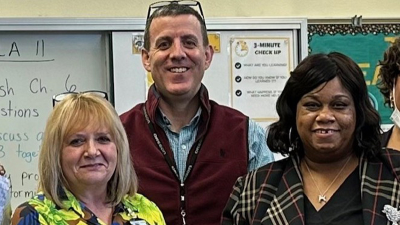 Josh Adams and two others smiling and posing for a photo in front of a school white board