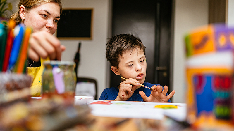 Individual with a student sitting at a table and painting