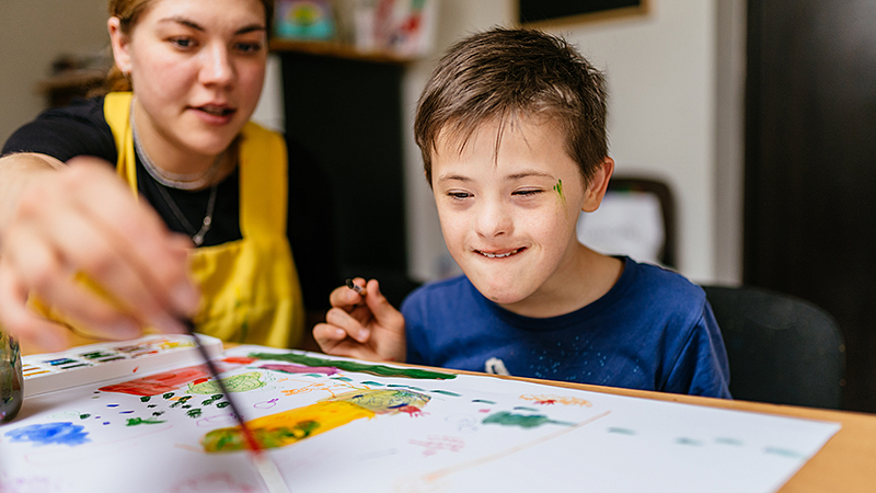 Individual with a student sitting at a table and painting