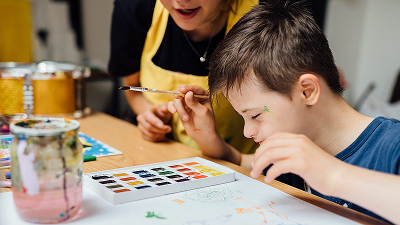 Individual with a student sitting at a table and painting