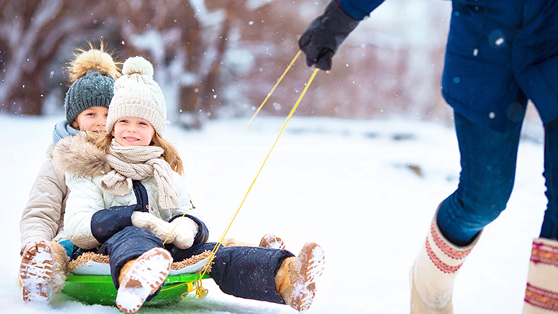 person pulling two young individuals in a sled on a snow covered ground