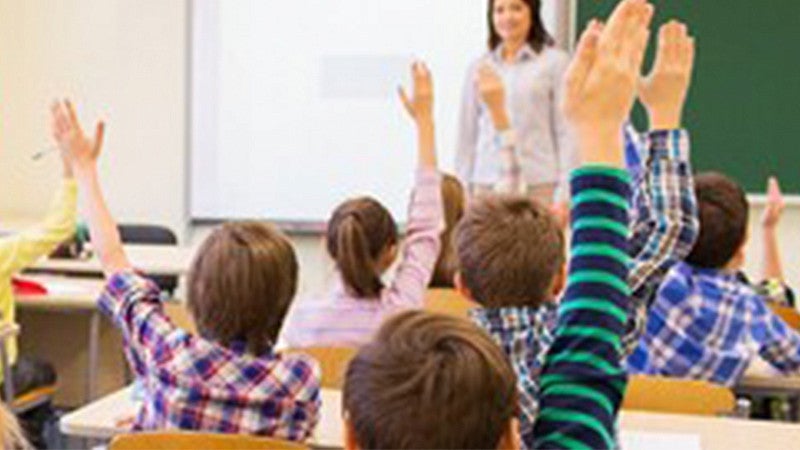 students raising their hands in a classroom with a teacher