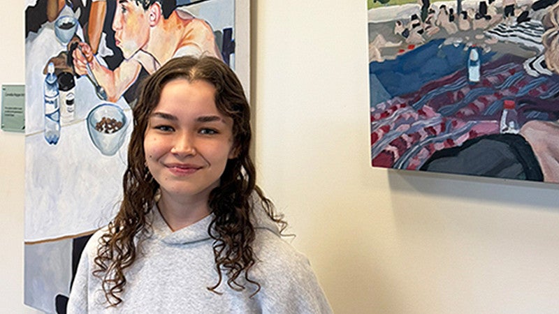 Ava Murakami standing in front of her artwork in the SAS office at the COE
