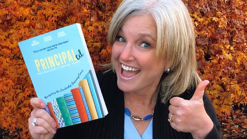 Kate Barker with one hand doing a thumbs up and the other hand holding her published book