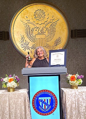 Kate Barker at a podium holding up an award certificate and trophy 