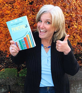 Kate Barker with one hand doing a thumbs up and the other hand holding her published book