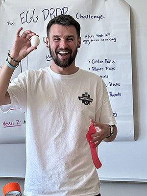 Alex Walker in a classroom holding up an egg for Egg Drop Challenge