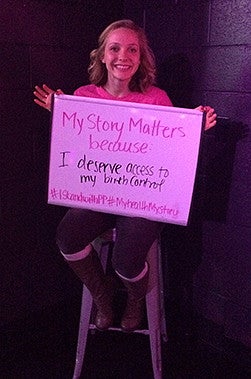 Leah Schluter sitting on a ladder holding a poster