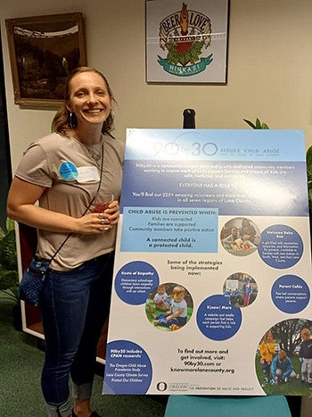 Leah Schluter standing next to a 90 x 30.org program poster
