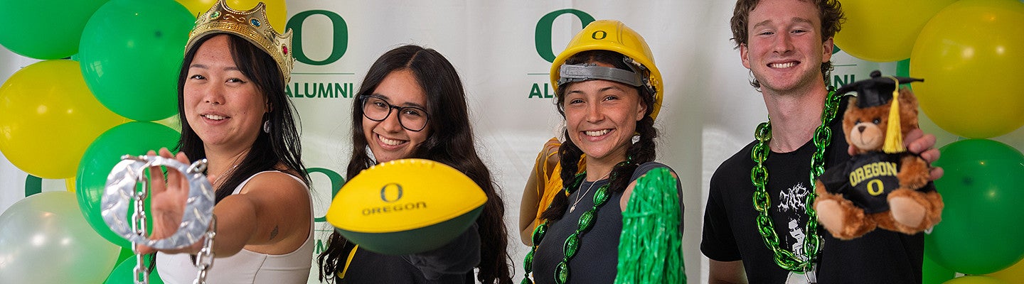 individuals in University of Oregon branded gear standing in front of an alumni banner