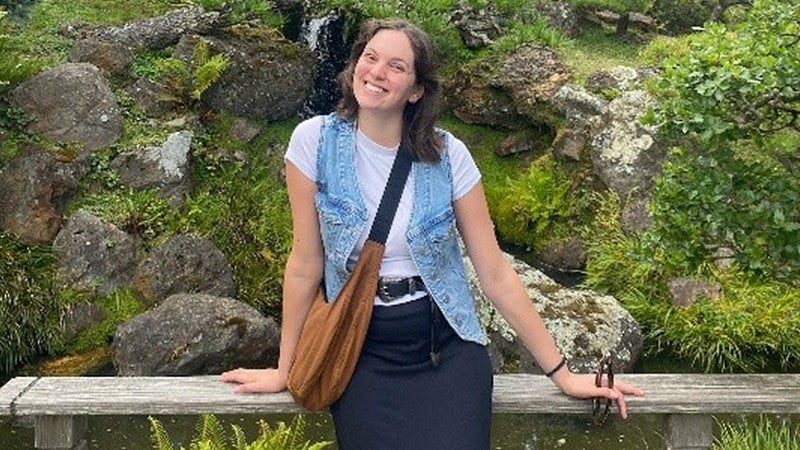 Lilly Gaven leaning against a wooden fence with a moss covered rocky background