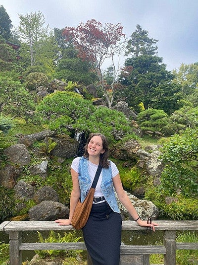 Alum Lilly Gaven leaning against a wooden fence in front of a wooded area
