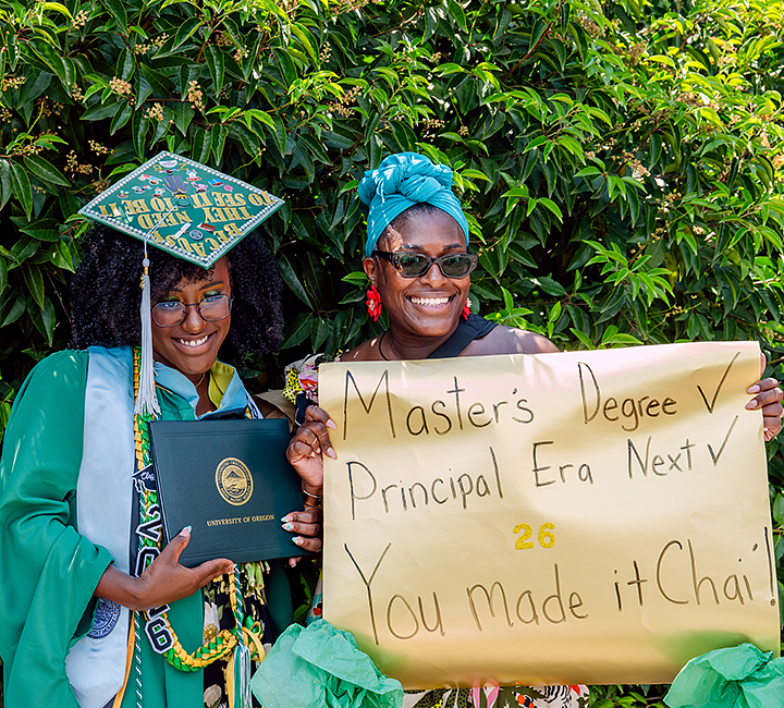 UO grad holding diploma next to an individual holding a sign