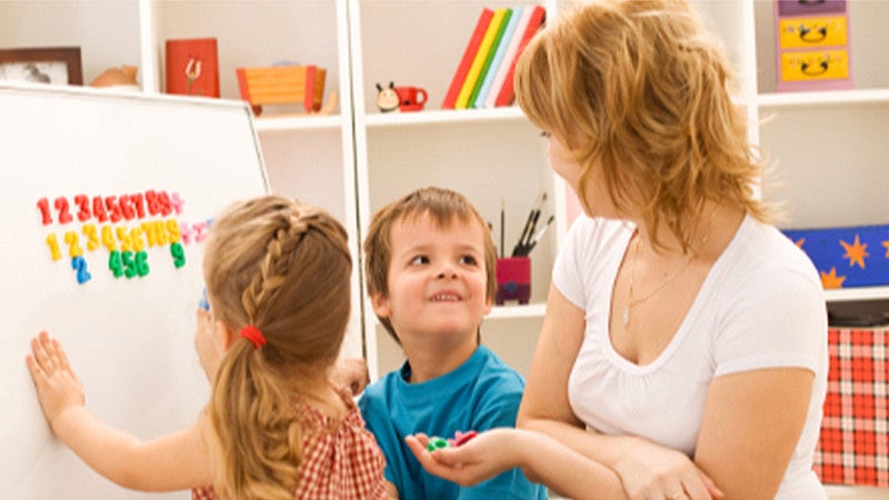 Teacher sitting with young individuals in front of a white board with magnet numbers