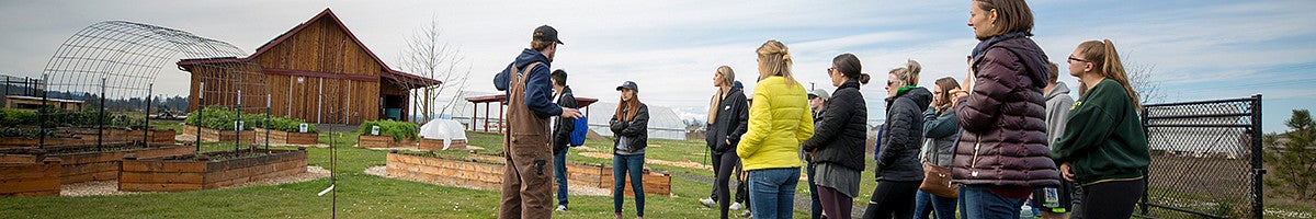 group of students on a farm listening to a farmer speak