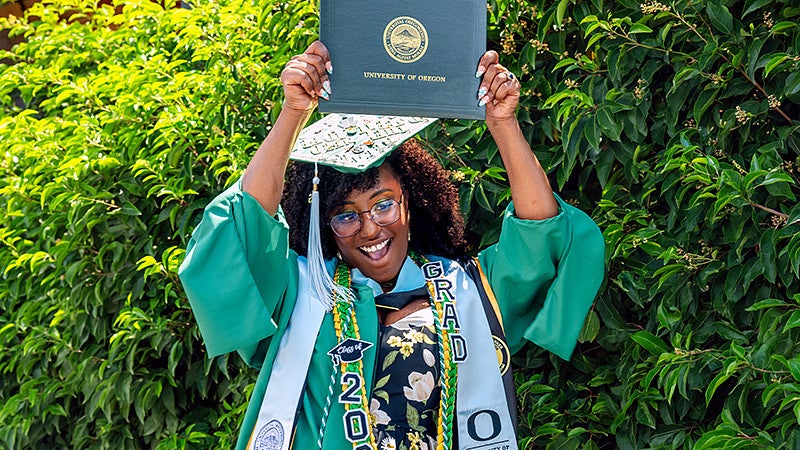 College of Education graduate in regalia holding up diploma