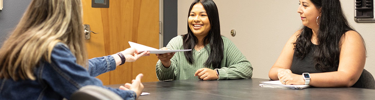three individuals sitting at a table one is receiving a paper from another