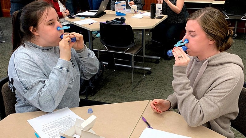 CDS students in a classroom sitting at a table testing blowing devices