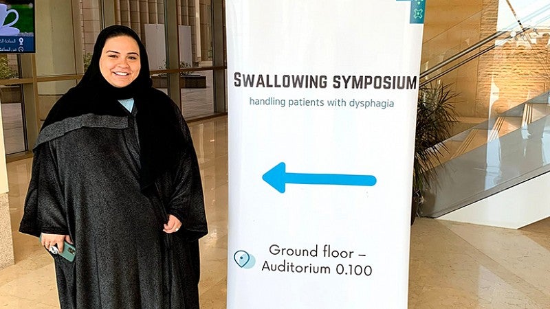 CDS student at a swallowing conference standing in front of the sign