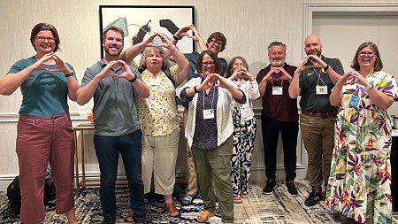 group of COE faculty past and present using their hands to form an O