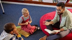 Adult sitting on floor speaking with young individuals