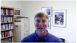 professor John Seeley speaking to the camera wearing a blue shirt