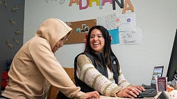 Adriana Alvarez smiling in a classroom with a student who is wearing a beige hoodie