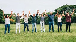 group of individuals standing in a field of grass holding hands raised up in the air