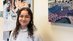 Ava Murakami standing in front of her artwork in the SAS office at the COE