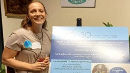 Leah Schluter standing next to a 90 x 30.org program poster