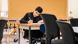 individual sitting at a desk writing on a piece of paper in classroom setting