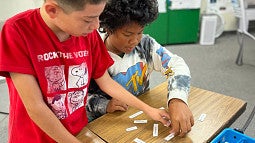 two young individuals working on a word puzzle on top of a classroom table
