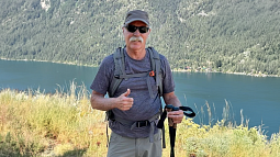 Bruce Waltz standing in an outdoor setting in hiking gear giving a thumbs up sign
