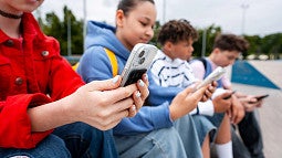 Young children sitting down holding cell phones