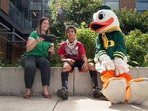 A female working with a young boy sitting with the Oregon Duck